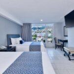 Habitación de hotel con dos camas, televisión de pantalla plana y balcón con vista a la ciudad